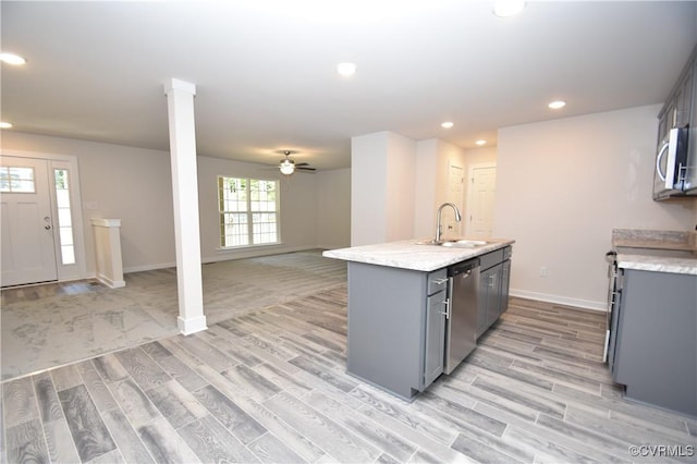 kitchen with sink, appliances with stainless steel finishes, gray cabinetry, an island with sink, and light wood-type flooring