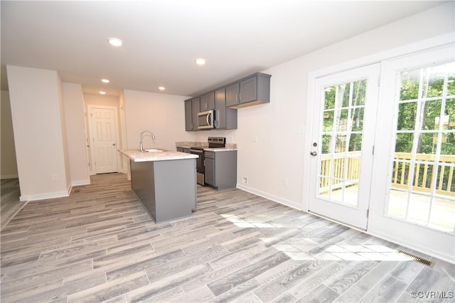 kitchen with sink, light hardwood / wood-style flooring, a kitchen island with sink, stainless steel appliances, and light stone counters