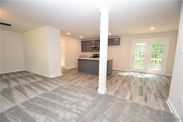 unfurnished living room with light colored carpet, sink, and decorative columns