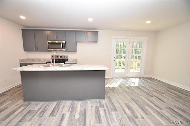 kitchen featuring stainless steel appliances, a kitchen island with sink, and light stone counters