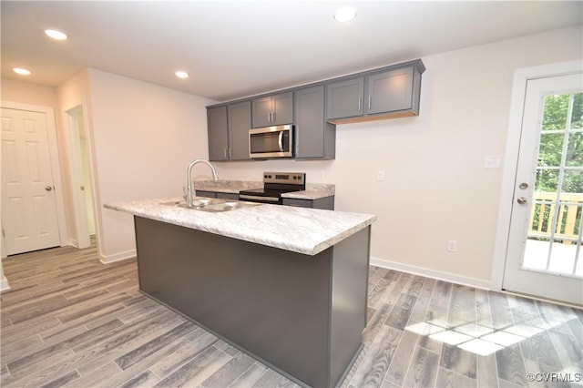 kitchen featuring sink, light hardwood / wood-style flooring, gray cabinets, appliances with stainless steel finishes, and a center island with sink