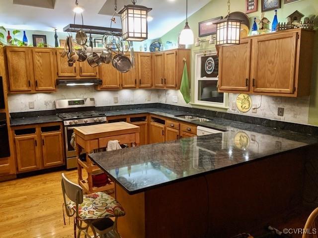 kitchen featuring stainless steel gas stove, hanging light fixtures, kitchen peninsula, dark stone counters, and light hardwood / wood-style floors