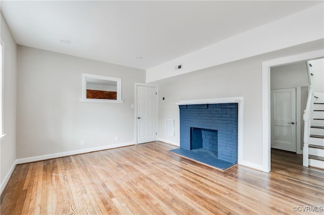 unfurnished living room featuring light hardwood / wood-style floors and a brick fireplace