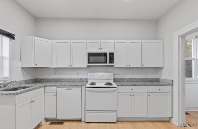 kitchen featuring sink, white cabinets, light stone countertops, white appliances, and light hardwood / wood-style flooring