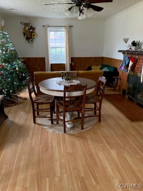 dining room featuring a fireplace, light hardwood / wood-style floors, a textured ceiling, and wood walls