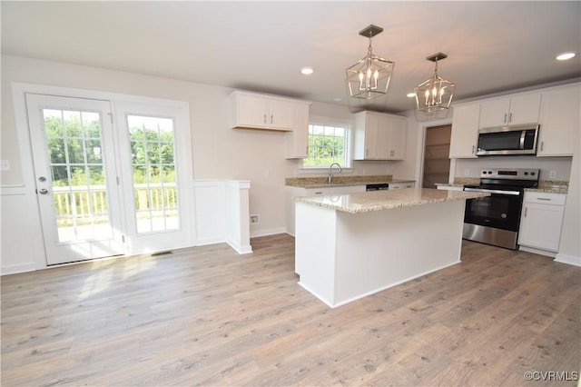 kitchen with stainless steel appliances, decorative light fixtures, a kitchen island, and white cabinets