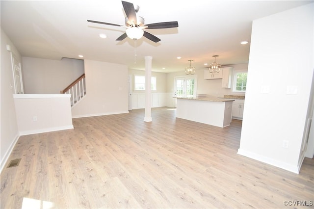 unfurnished living room featuring ceiling fan with notable chandelier and light wood-type flooring