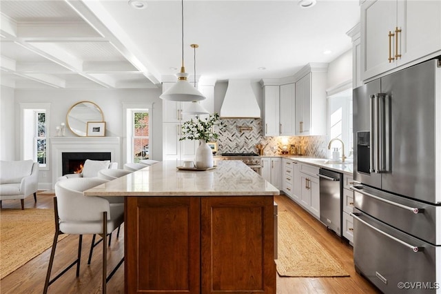 kitchen with hanging light fixtures, a center island, high end appliances, light stone countertops, and custom range hood