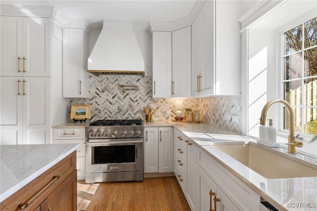 kitchen with sink, premium range hood, high end range, light stone counters, and white cabinets