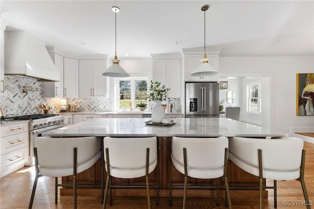 kitchen featuring pendant lighting, white cabinetry, premium appliances, custom range hood, and a kitchen island