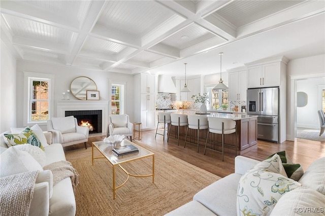 living room featuring coffered ceiling, a fireplace, beamed ceiling, and light wood-type flooring