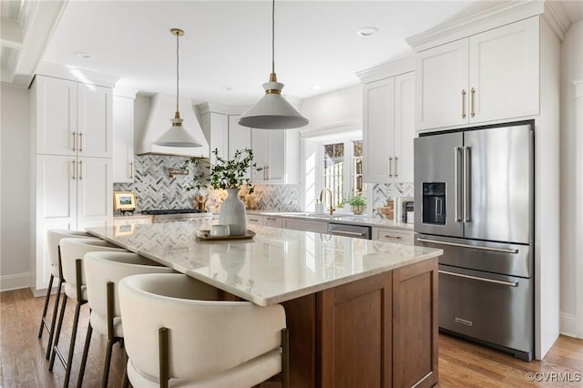 kitchen with a kitchen island, white cabinetry, hanging light fixtures, light stone counters, and stainless steel appliances