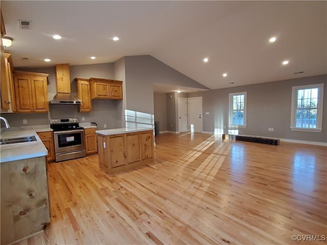 kitchen featuring wall chimney exhaust hood, sink, stainless steel electric range oven, a center island, and light wood-type flooring