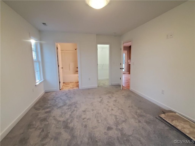 unfurnished bedroom with a walk in closet, connected bathroom, carpet, and a closet