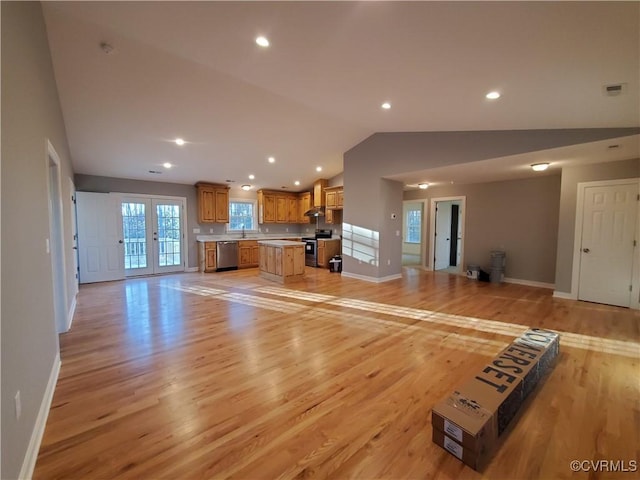 unfurnished living room featuring french doors, lofted ceiling, sink, and light hardwood / wood-style floors