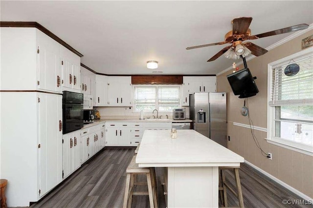 kitchen with crown molding, black oven, a breakfast bar, white cabinets, and stainless steel fridge with ice dispenser