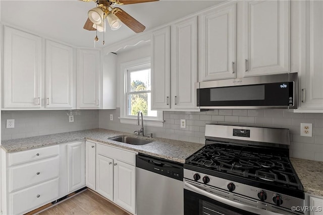 kitchen with stainless steel appliances, white cabinetry, sink, and light stone counters