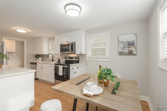 kitchen with sink, white cabinetry, light wood-type flooring, stainless steel appliances, and backsplash