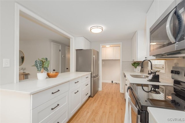 kitchen with sink, light hardwood / wood-style flooring, white cabinetry, stainless steel appliances, and decorative backsplash