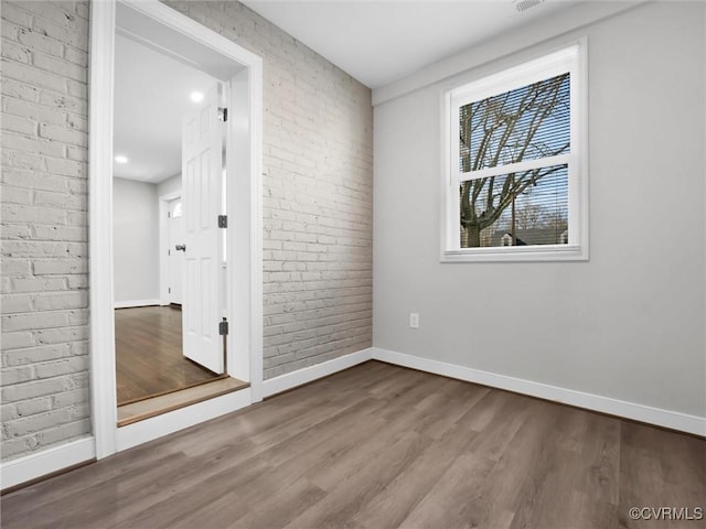 unfurnished room with hardwood / wood-style flooring and brick wall