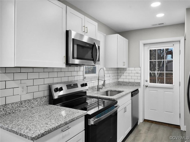 kitchen featuring white cabinetry, sink, light stone counters, stainless steel appliances, and light wood-type flooring