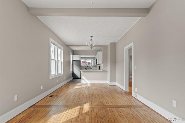 unfurnished living room with an inviting chandelier, sink, and light hardwood / wood-style floors