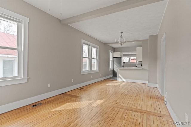 unfurnished living room featuring beam ceiling, a chandelier, sink, and light wood-type flooring