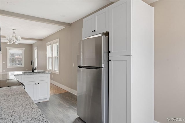 kitchen with sink, stainless steel fridge, light stone counters, white cabinets, and light wood-type flooring