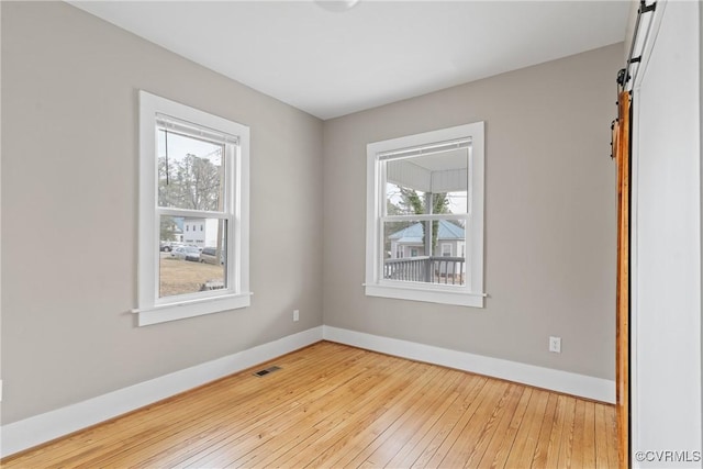 empty room with a barn door, a healthy amount of sunlight, and light wood-type flooring