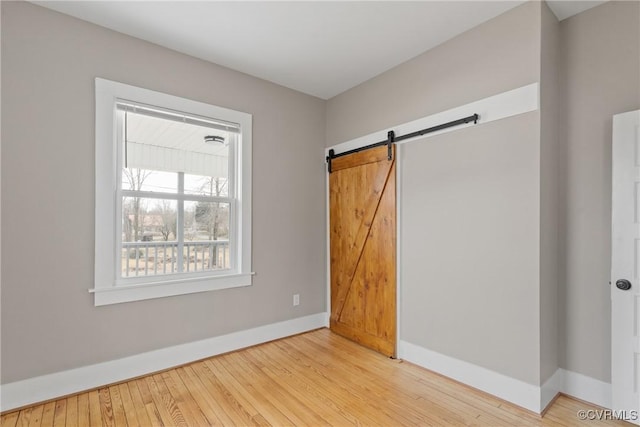 unfurnished bedroom with a barn door and light hardwood / wood-style flooring