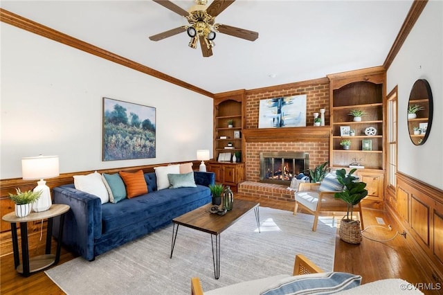 living room with a brick fireplace, hardwood / wood-style flooring, crown molding, and built in features