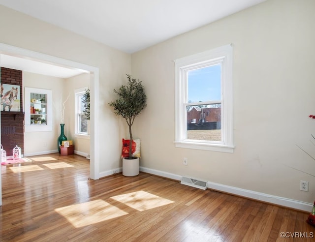 empty room featuring a brick fireplace, wood finished floors, visible vents, and baseboards