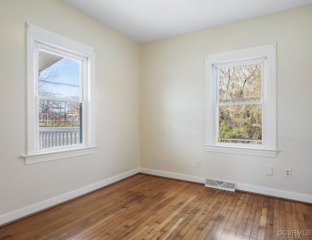 unfurnished room with wood-type flooring, visible vents, and baseboards