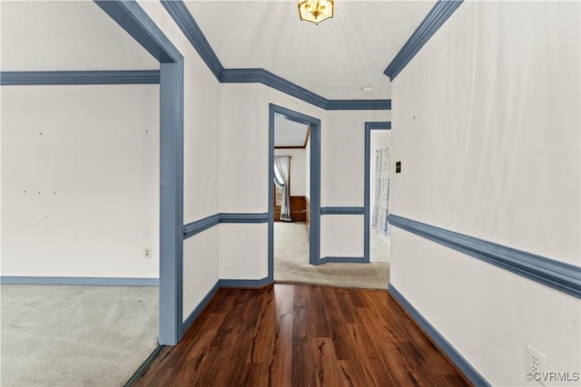 interior space featuring dark carpet, baseboards, dark wood-type flooring, and crown molding