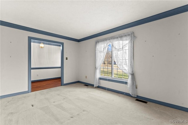 empty room with baseboards, visible vents, light colored carpet, and ornamental molding