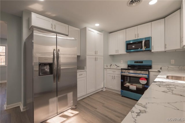 kitchen with stainless steel appliances, white cabinetry, light stone countertops, and light hardwood / wood-style floors