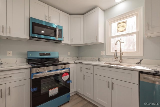 kitchen with white cabinetry, stainless steel appliances, light stone countertops, and sink