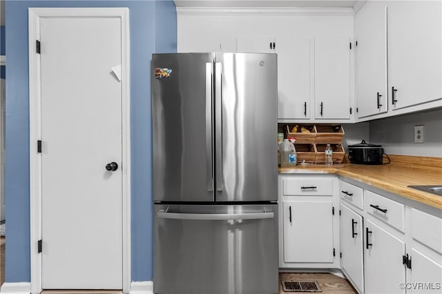 kitchen with crown molding, white cabinets, and stainless steel refrigerator