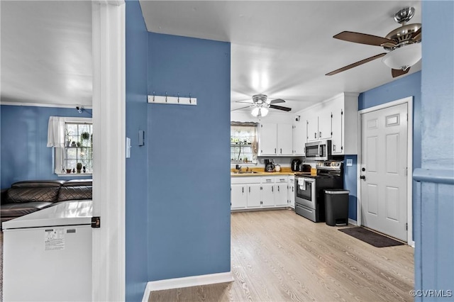 kitchen featuring sink, light hardwood / wood-style flooring, ceiling fan, stainless steel appliances, and white cabinets