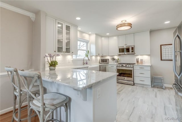 kitchen with stainless steel appliances, glass insert cabinets, white cabinets, a peninsula, and a kitchen breakfast bar