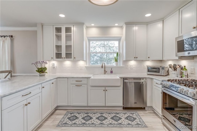 kitchen with a sink, white cabinetry, appliances with stainless steel finishes, light stone countertops, and glass insert cabinets