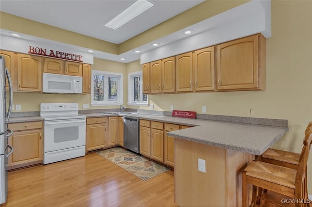 kitchen featuring sink, a breakfast bar area, appliances with stainless steel finishes, kitchen peninsula, and light hardwood / wood-style floors