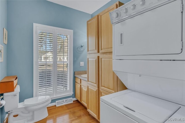 laundry room with stacked washer and dryer and light hardwood / wood-style flooring