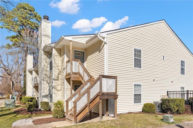 rear view of property with central AC unit, a chimney, stairway, and a yard