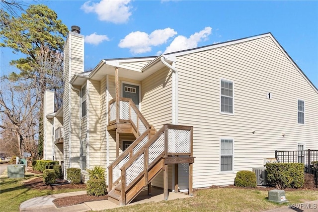 rear view of house featuring a chimney, central air condition unit, a lawn, and stairway