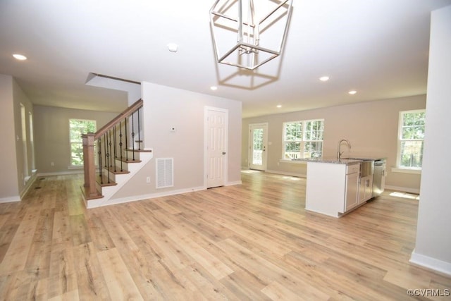 kitchen with light stone countertops, sink, pendant lighting, and light wood-type flooring