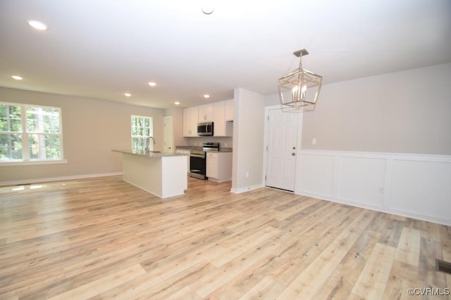 kitchen with hanging light fixtures, stainless steel appliances, white cabinets, and light wood-type flooring