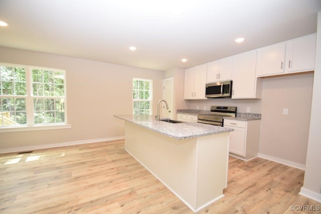 kitchen with white cabinetry, sink, light stone counters, stainless steel appliances, and a center island with sink