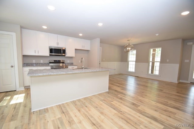 kitchen with sink, white cabinetry, appliances with stainless steel finishes, an island with sink, and light stone countertops