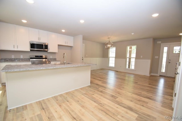 kitchen featuring sink, white cabinetry, an island with sink, stainless steel appliances, and light stone countertops